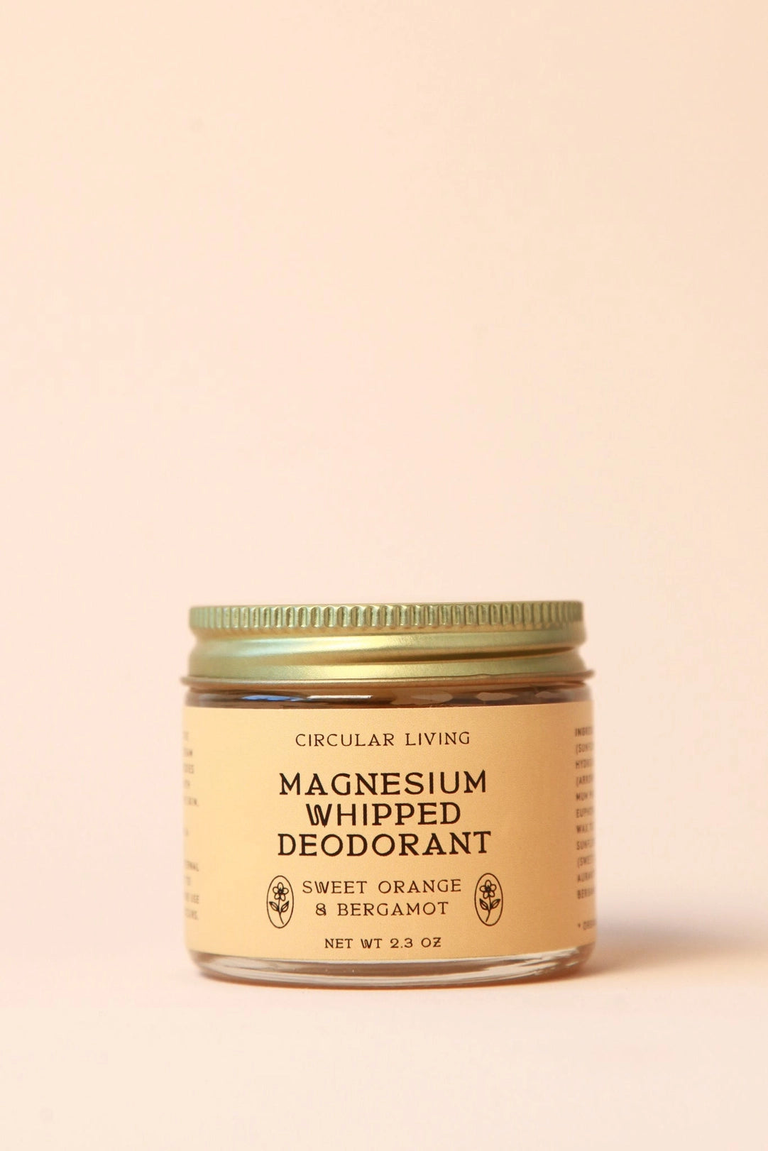 Circular Living Magnesium Whipped Deodorant, Sweet Orange & Bergamot in a small clear glass jar with orange label and gold screw lid, centered against a warm pale-peach background.