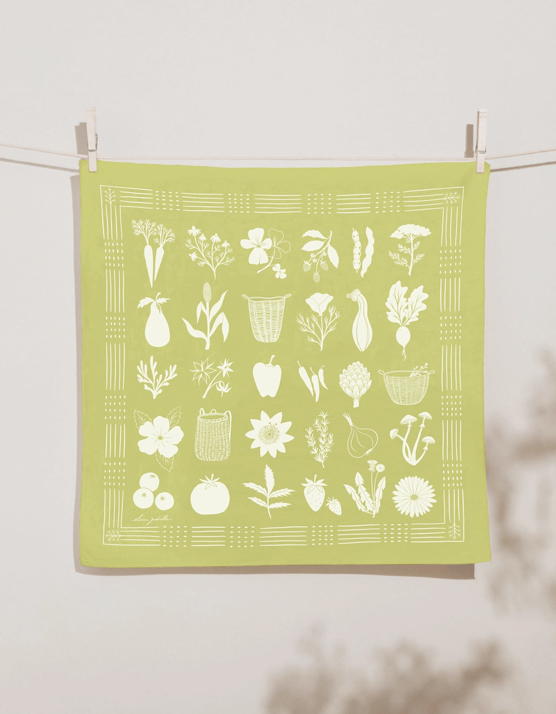 Light chartreuse-green Elana Gabrielle Forage Bandana clipped to a clothesline, screen printed in white with baskets, vegetables, flowers, herbs, mushrooms and gathered garden produce.
