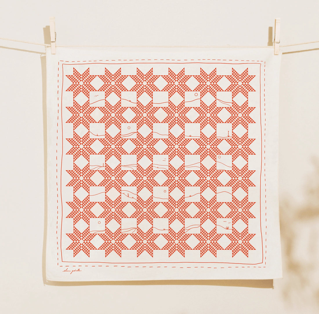 Cream square Quilt Bandana clipped to a clothesline, printed in brick red with a repeating geometric patchwork pattern of eight-pointed stars, diamonds and small landscape-like line details.