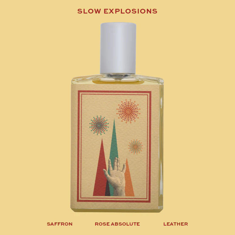 Imaginary Authors Slow Explosions clear rectangular perfume bottle with a white cylindrical cap and an illustrated label of a raised hand, colorful triangular forms and circular bursts on a pale yellow background.