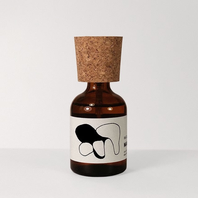 Marlou Héliodose eau de parfum in a squat amber-brown apothecary bottle with wide natural cork cap and a white wraparound label printed with abstract black line-and-shape artwork on pale gray.